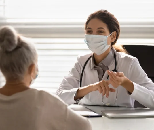Doctor wearing a mask talking to a patient wearing a mask.